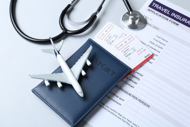 Photo of Medical tourism. Travel insurance application form, stethoscope, plane model, passport and flight tickets on light background