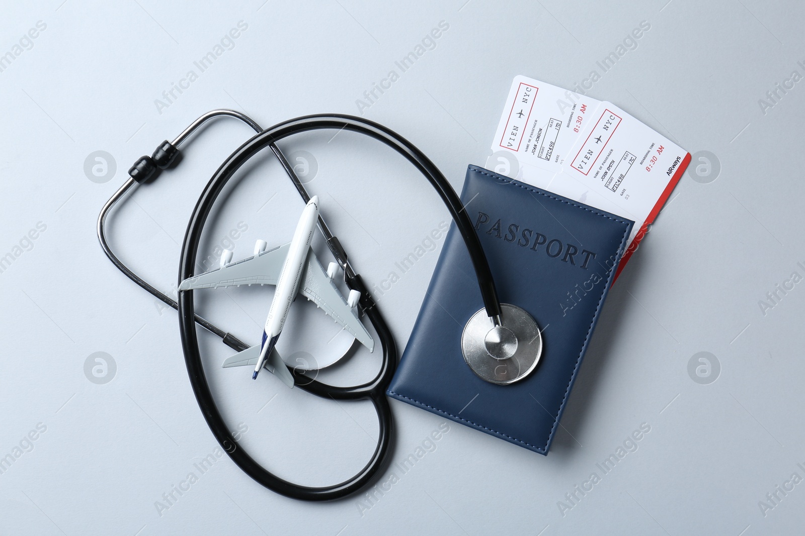 Photo of Medical tourism. Stethoscope, plane model, passport and flight tickets on light blue background, flat lay