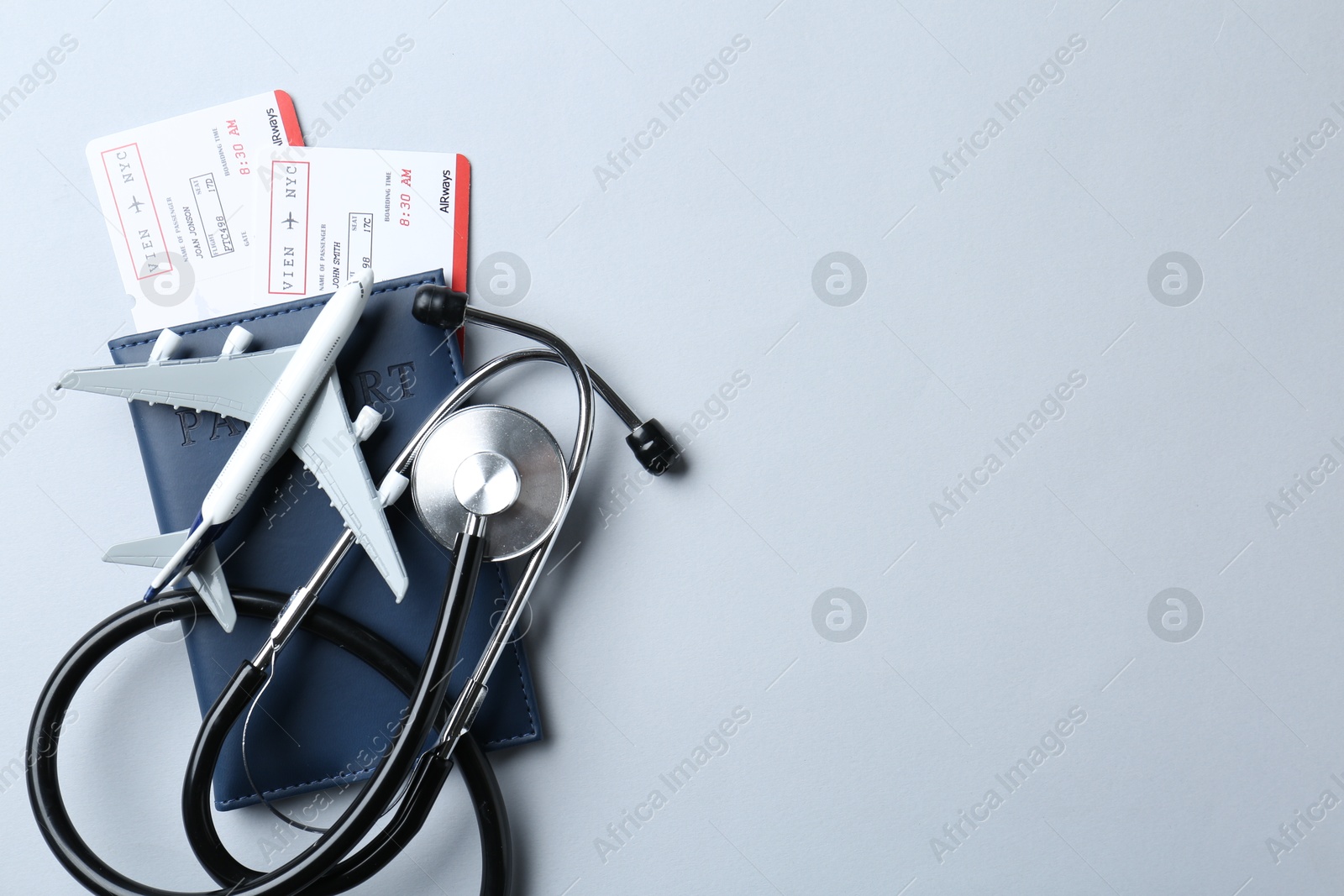 Photo of Medical tourism. Stethoscope, plane model, passport and flight tickets on light blue background, top view. Space for text