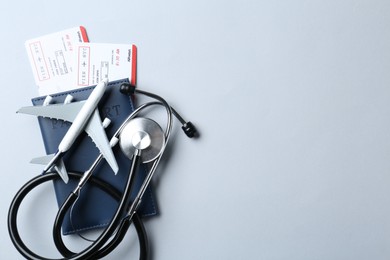 Photo of Medical tourism. Stethoscope, plane model, passport and flight tickets on light blue background, top view. Space for text