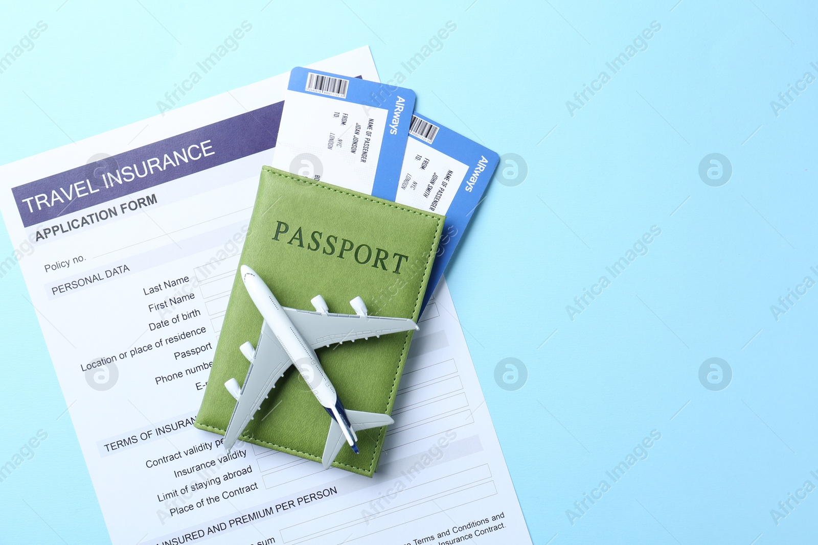 Photo of Medical tourism. Travel insurance application form, plane model, flight tickets and passport on light blue background, flat lay. Space for text