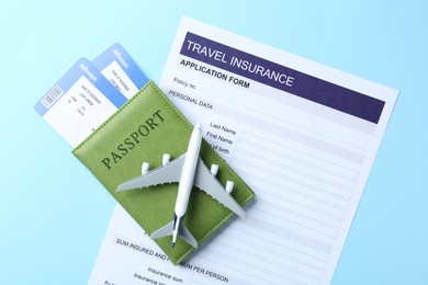 Photo of Medical tourism. Travel insurance application form, plane model, flight tickets and passport on light blue background, flat lay