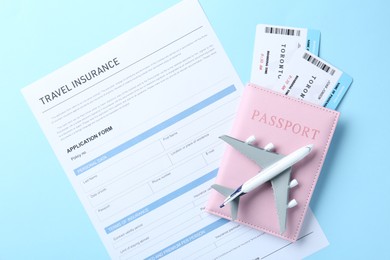 Photo of Medical tourism. Travel insurance application form, plane model, flight tickets and passport on light blue background, top view