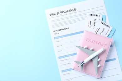 Photo of Medical tourism. Travel insurance application form, plane model, flight tickets and passport on light blue background, top view. Space for text