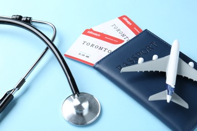 Photo of Medical tourism. Stethoscope, plane model, passport and flight tickets on light blue background, closeup