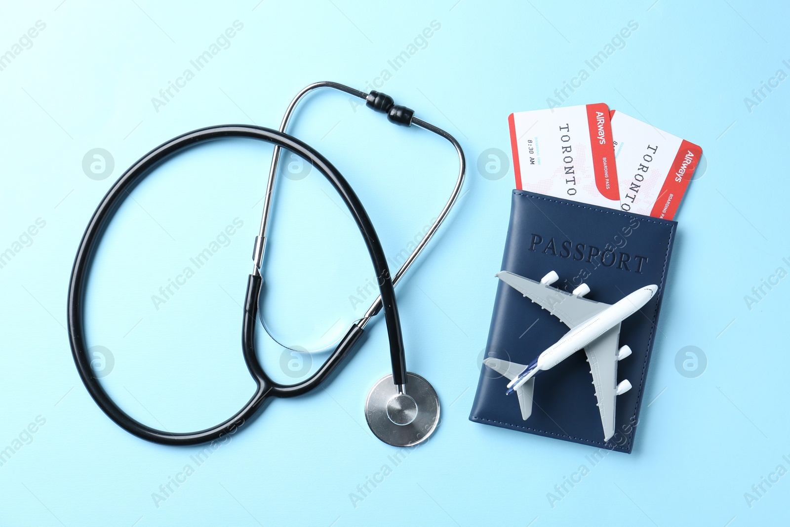 Photo of Medical tourism. Stethoscope, plane model, passport and flight tickets on light blue background, flat lay