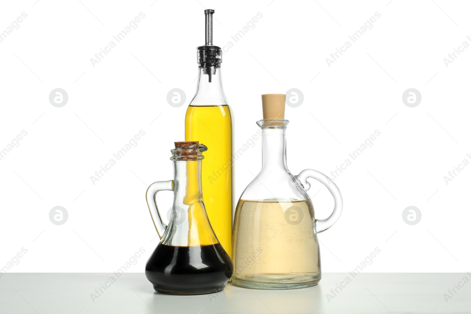 Photo of Oil and vinegars in bottles on table against white background