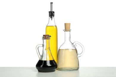 Photo of Oil and vinegars in bottles on table against white background