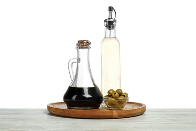 Photo of Vinegars in bottles and olives on wooden table against white background