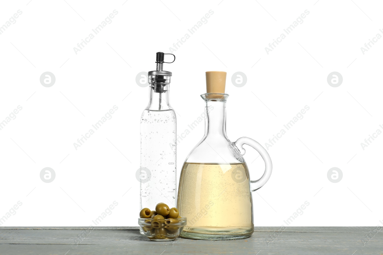 Photo of Vinegars in bottles and olives on grey wooden table against white background