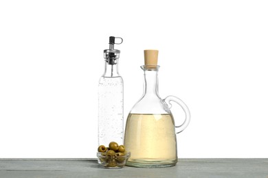 Photo of Vinegars in bottles and olives on grey wooden table against white background