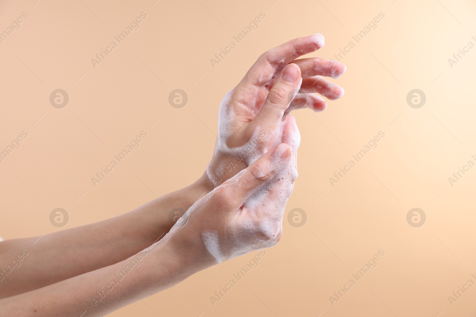 Photo of Woman washing hands with foaming soap on beige background, closeup. Hygiene