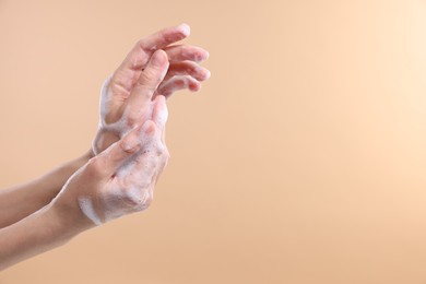 Photo of Woman washing hands with foaming soap on beige background, closeup with space for text. Hygiene