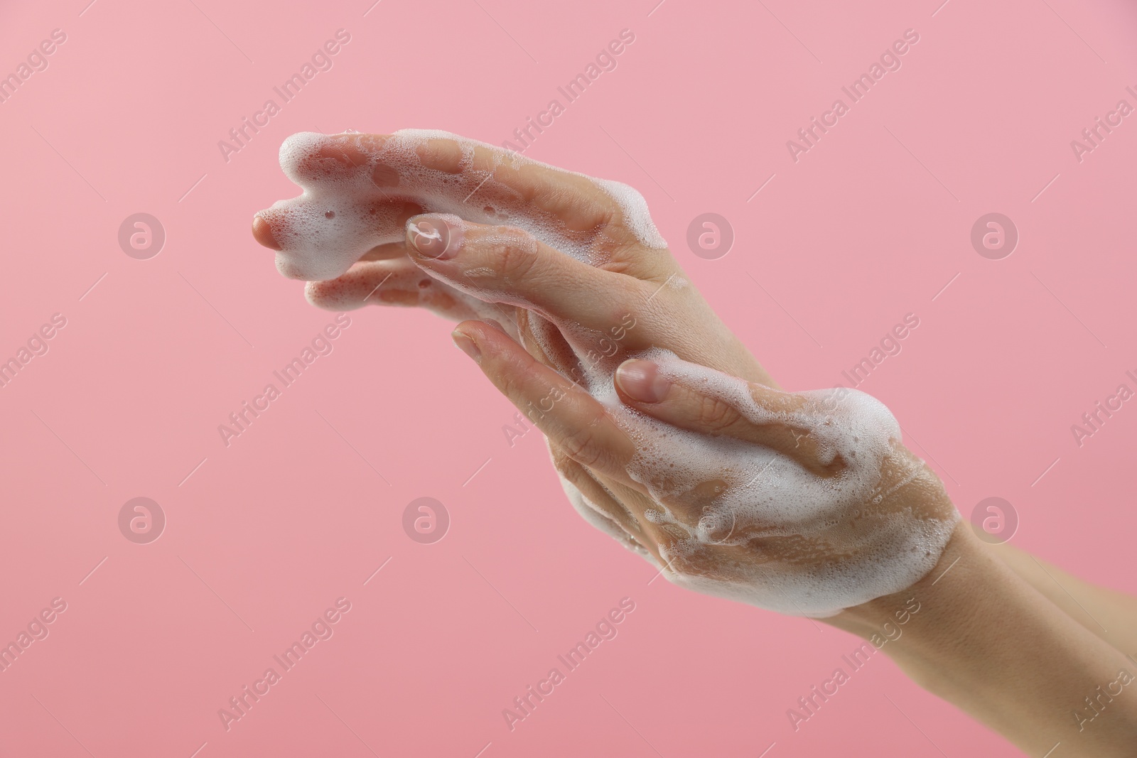 Photo of Woman washing hands with foaming soap on pink background, closeup. Hygiene