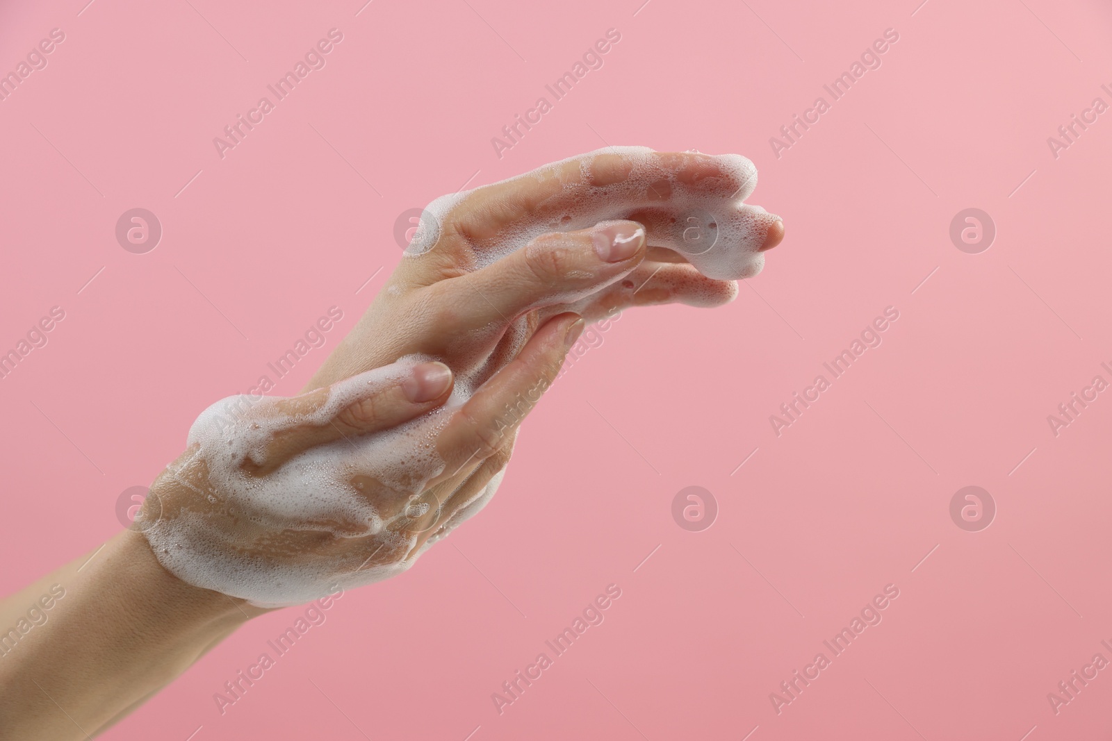 Photo of Woman washing hands with foaming soap on pink background, closeup. Hygiene