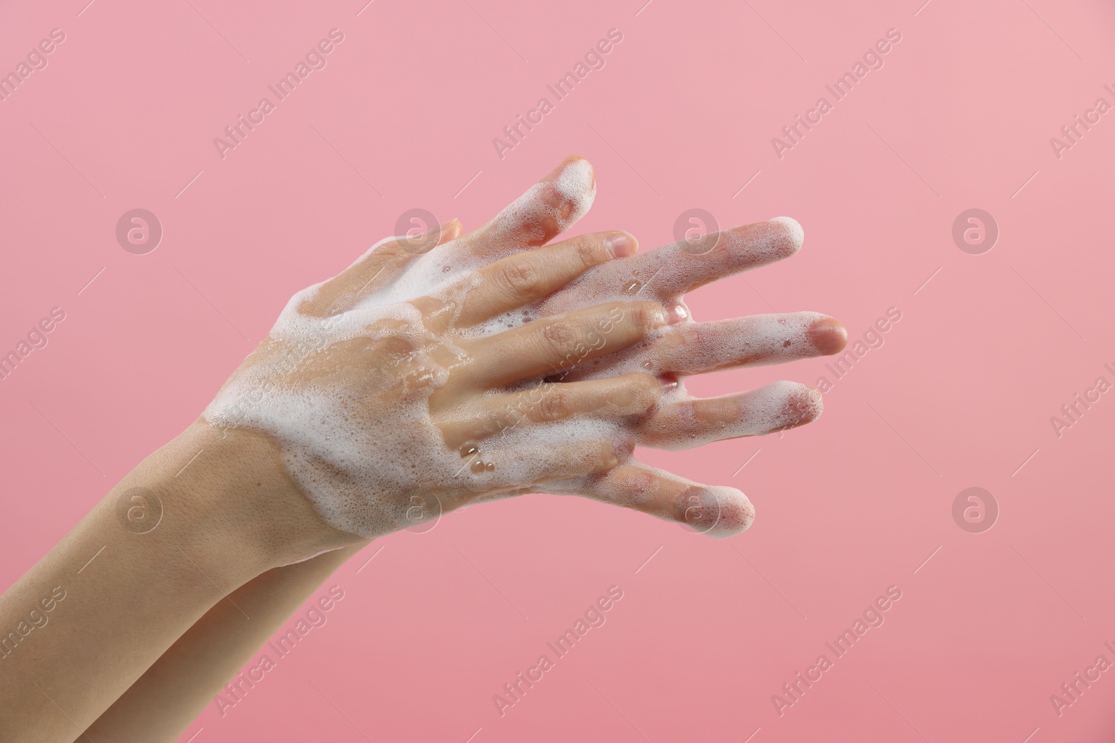 Photo of Woman washing hands with foaming soap on pink background, closeup. Hygiene