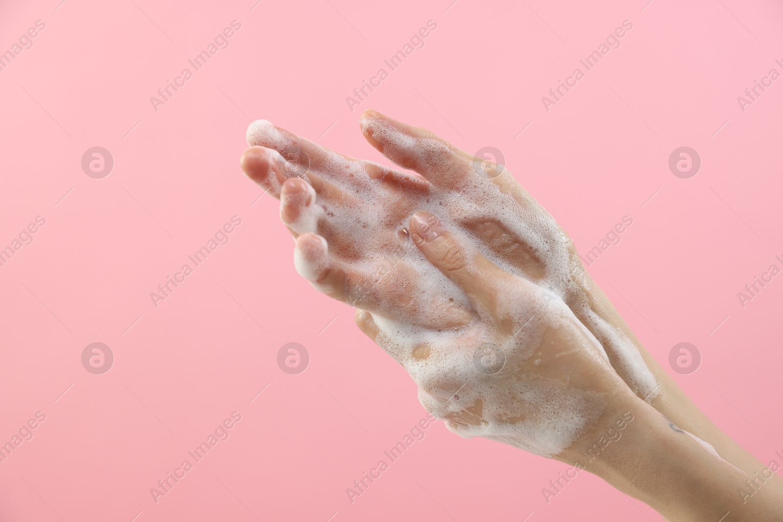 Photo of Woman washing hands with foaming soap on pink background, closeup. Hygiene