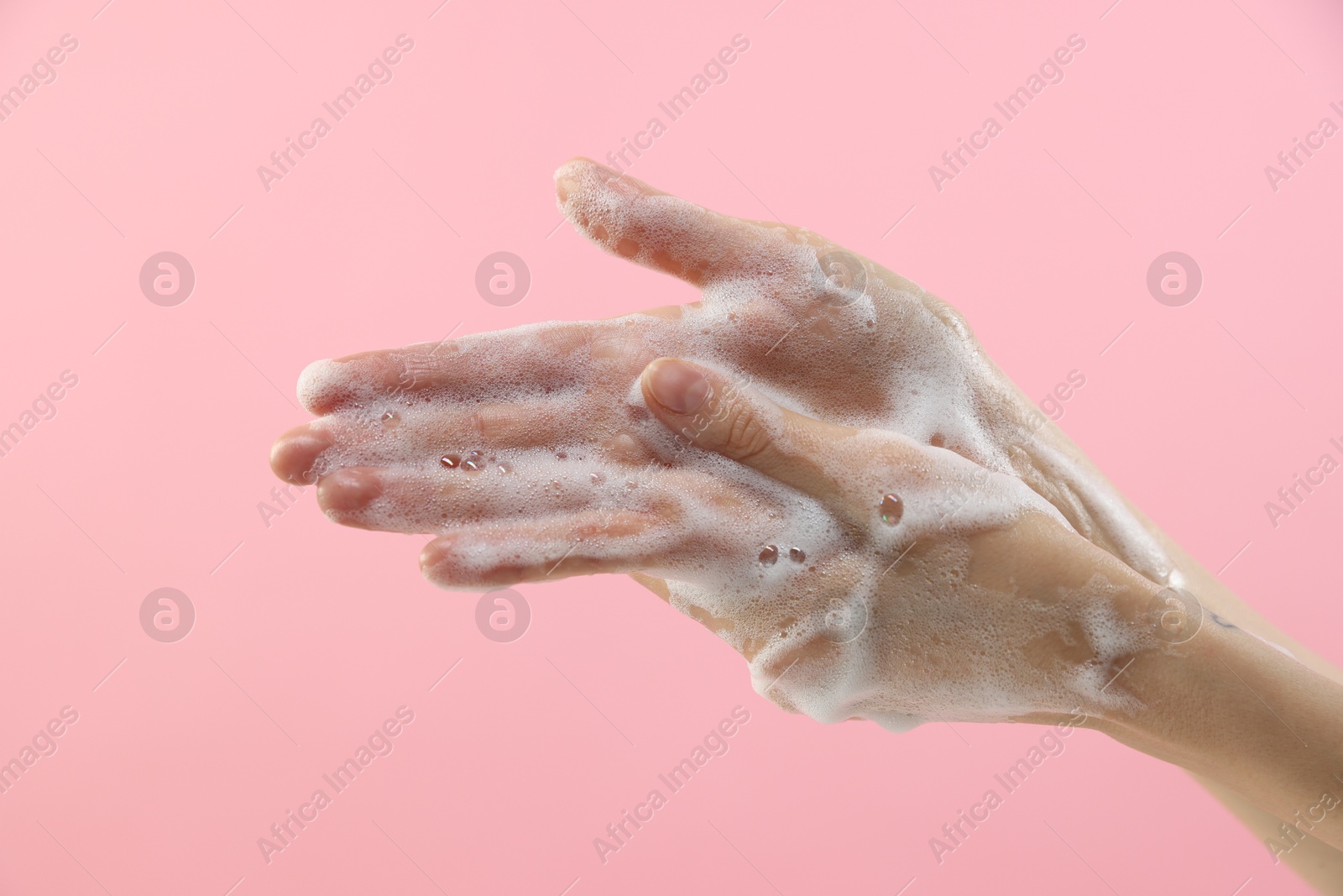 Photo of Woman washing hands with foaming soap on pink background, closeup. Hygiene