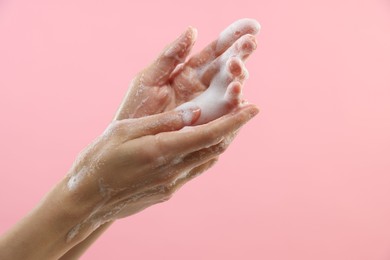 Photo of Woman washing hands with foaming soap on pink background, closeup with space for text. Hygiene