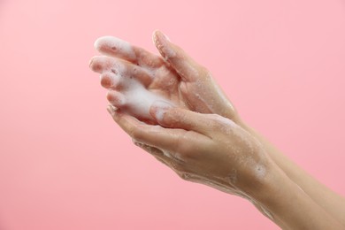 Photo of Woman washing hands with foaming soap on pink background, closeup. Hygiene