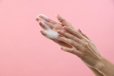 Photo of Woman washing hands with foaming soap on pink background, closeup with space for text. Hygiene