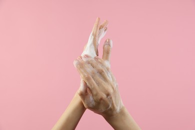 Photo of Woman washing hands with foaming soap on pink background, closeup. Hygiene