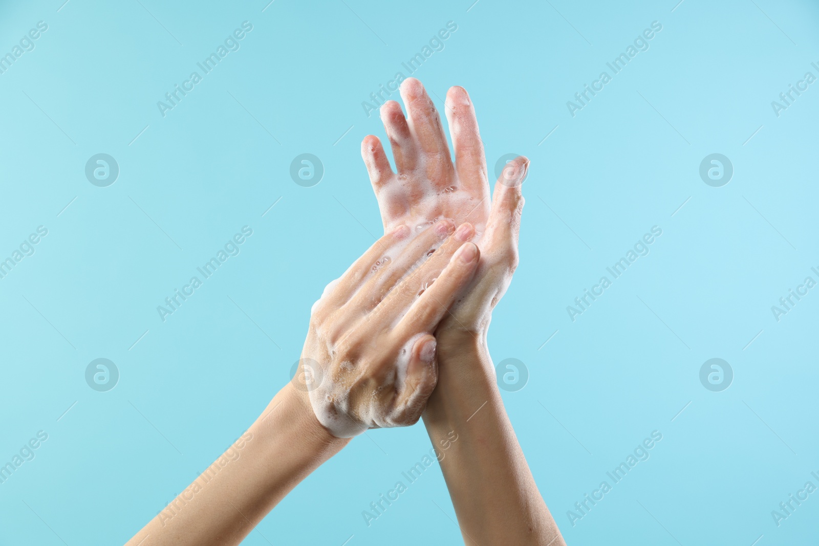 Photo of Woman washing hands with foaming soap on light blue background, closeup. Hygiene