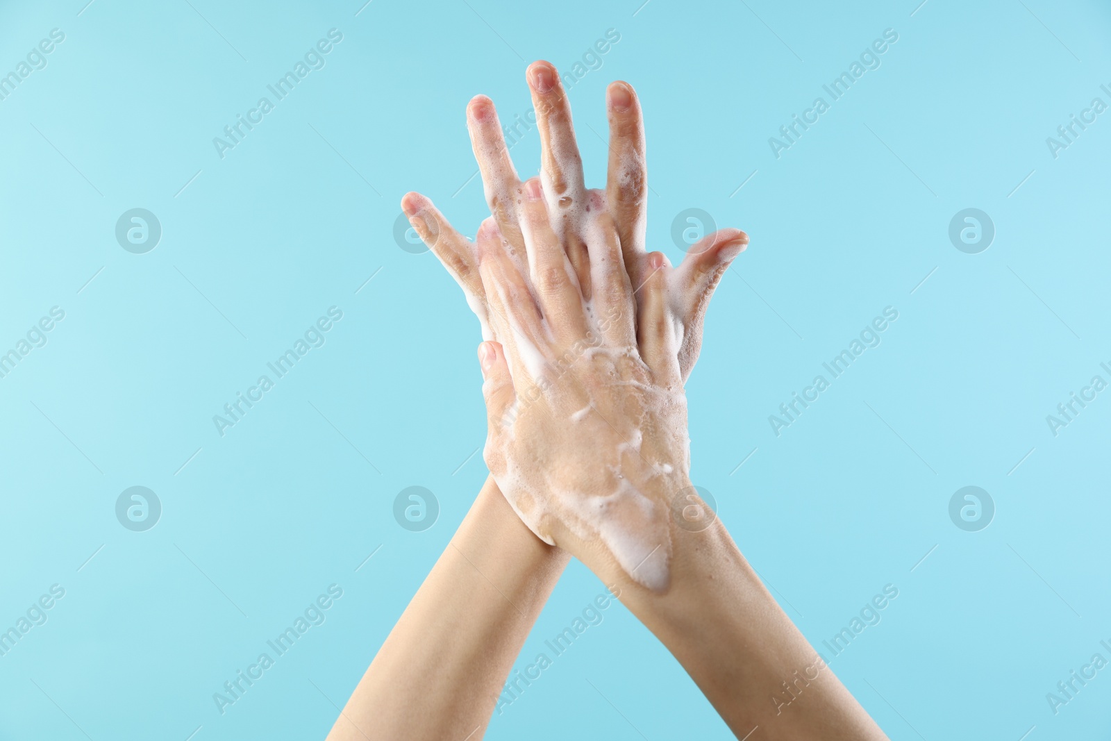 Photo of Woman washing hands with foaming soap on light blue background, closeup. Hygiene