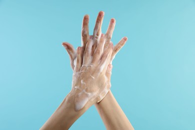 Photo of Woman washing hands with foaming soap on light blue background, closeup. Hygiene