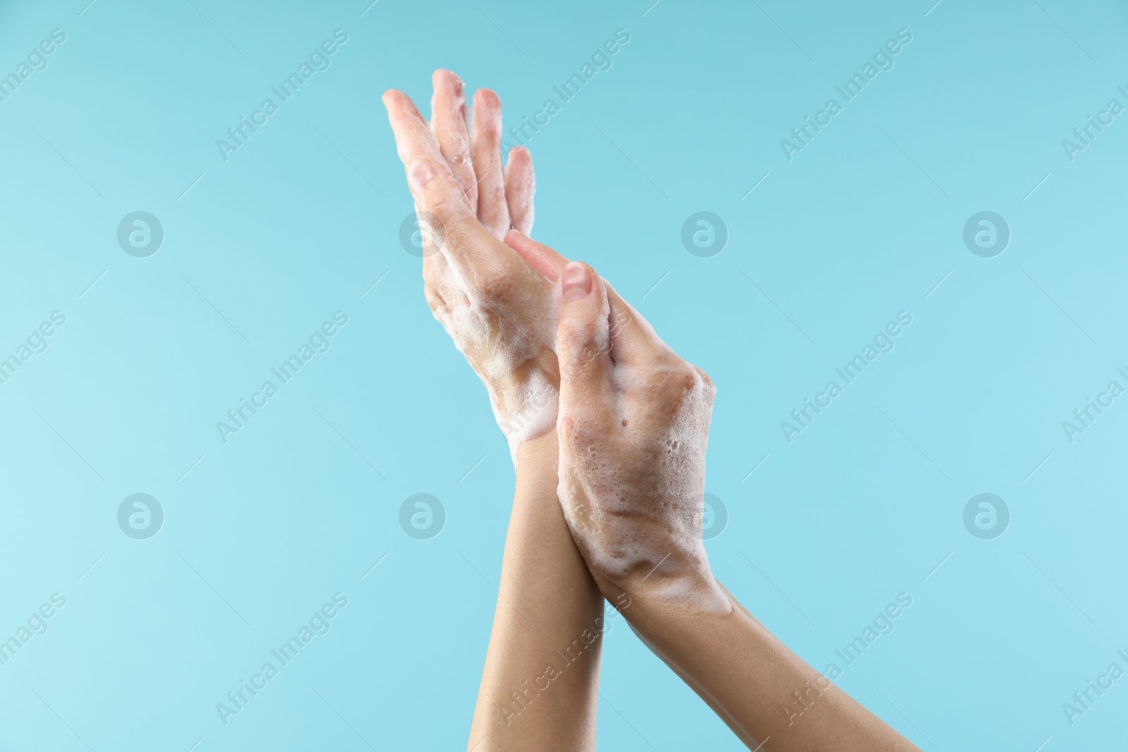 Photo of Woman washing hands with foaming soap on light blue background, closeup. Hygiene