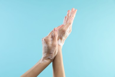 Photo of Woman washing hands with foaming soap on light blue background, closeup. Hygiene