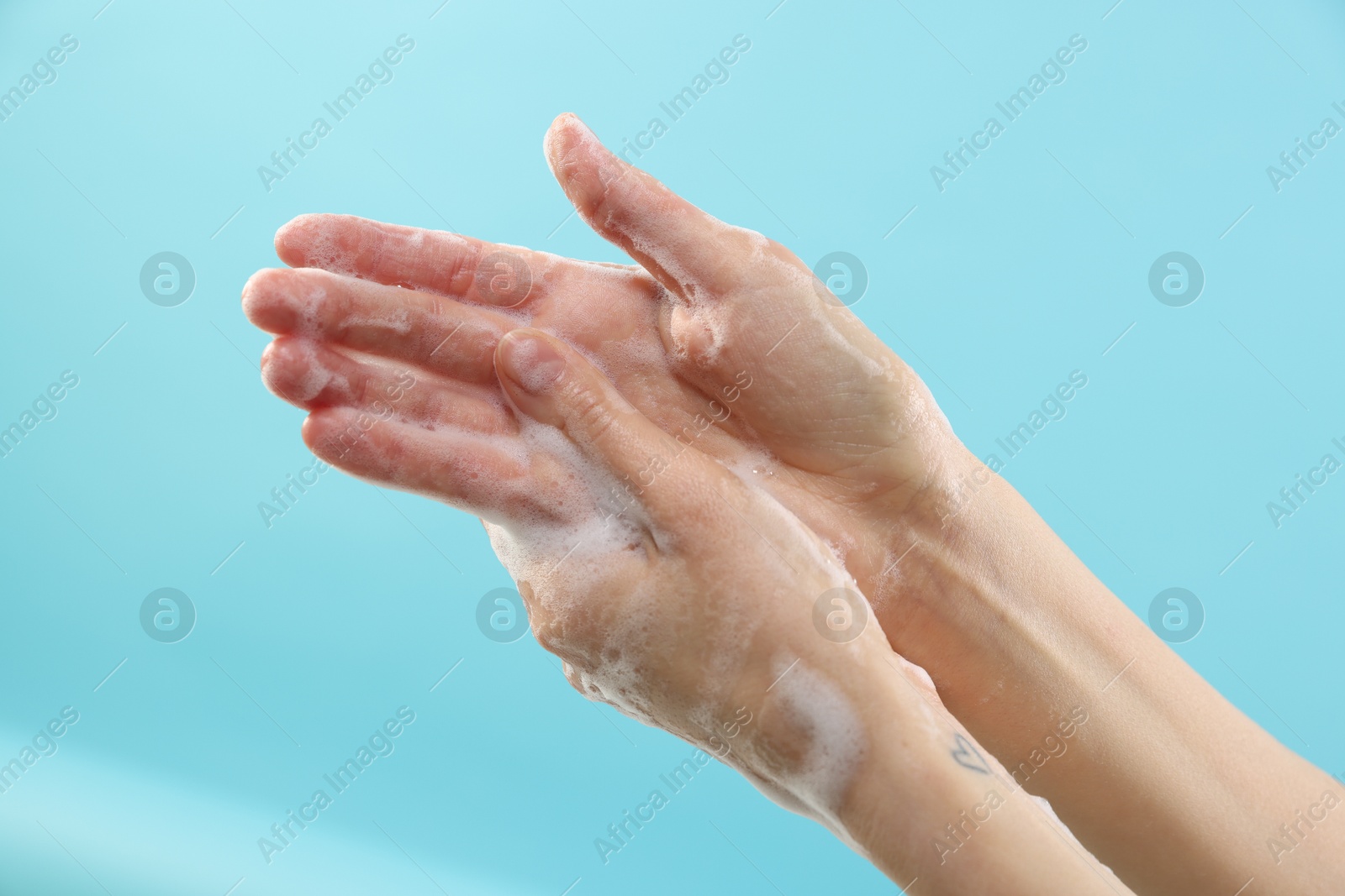 Photo of Woman washing hands with foaming soap on light blue background, closeup. Hygiene