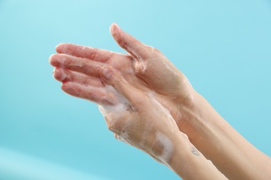 Photo of Woman washing hands with foaming soap on light blue background, closeup. Hygiene