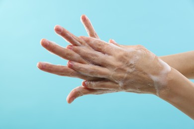 Photo of Woman washing hands with foaming soap on light blue background, closeup. Hygiene