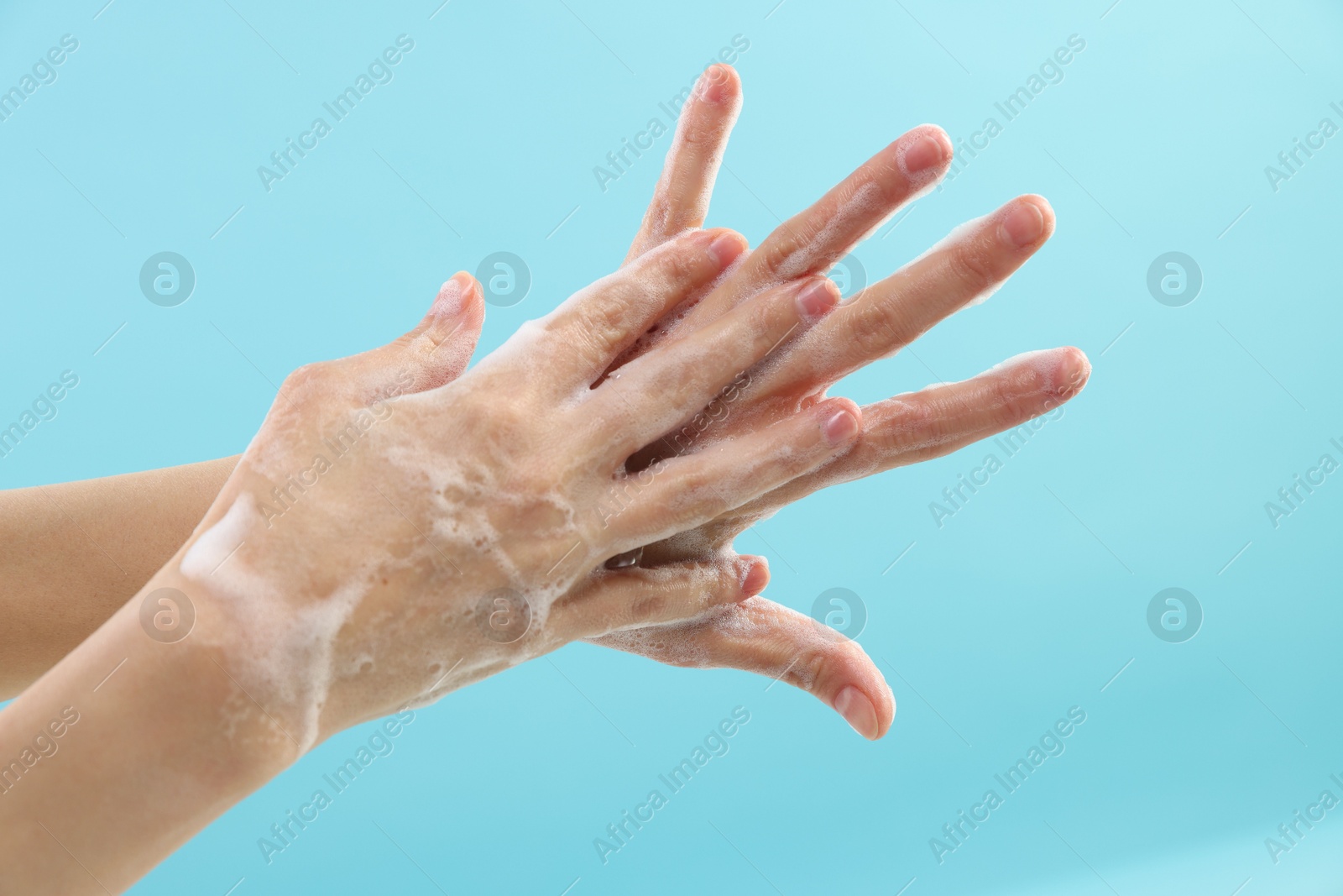 Photo of Woman washing hands with foaming soap on light blue background, closeup. Hygiene