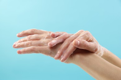 Photo of Woman washing hands with foaming soap on light blue background, closeup. Hygiene