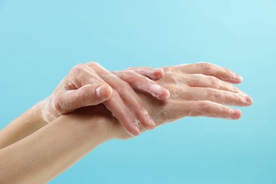 Photo of Woman washing hands with foaming soap on light blue background, closeup. Hygiene