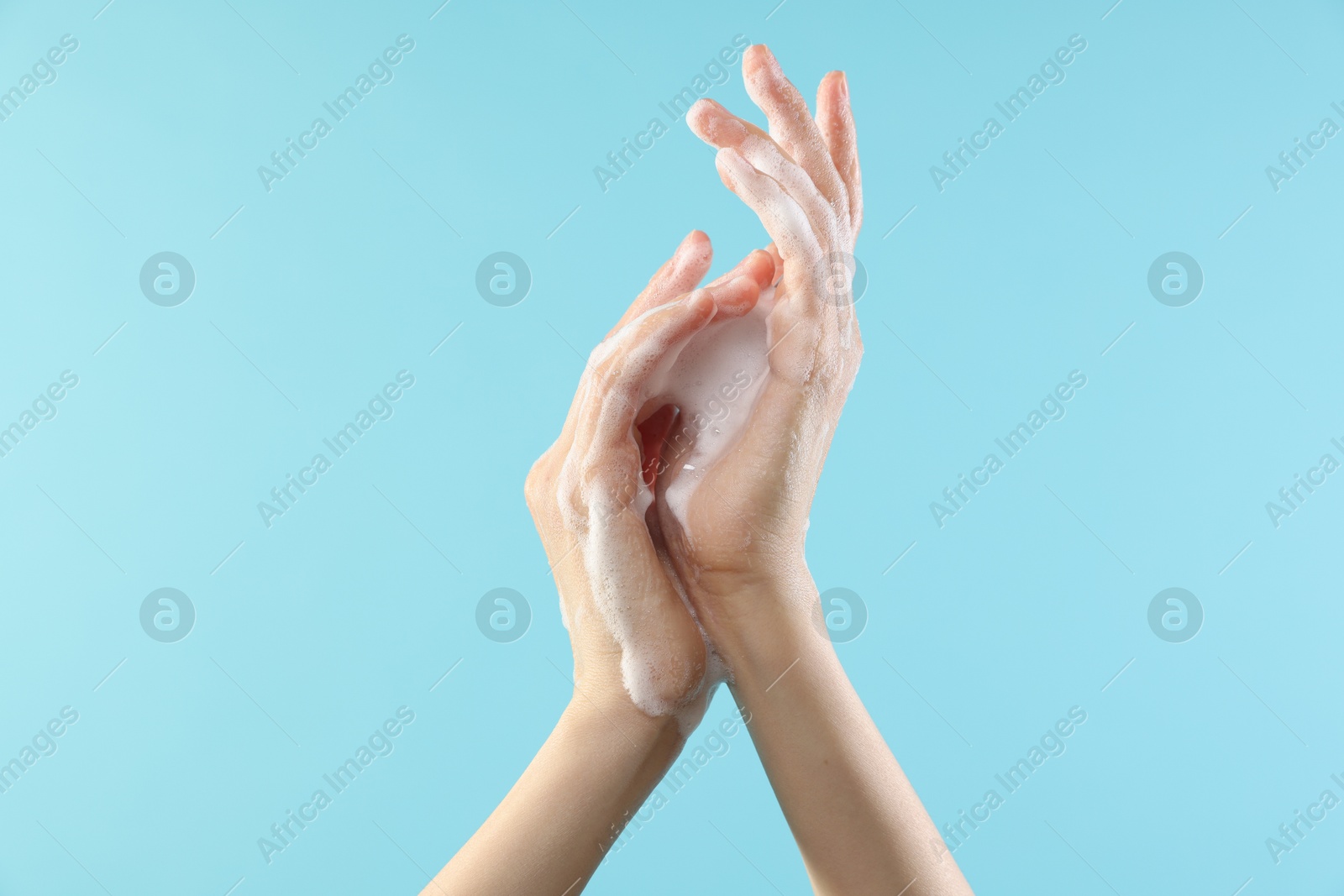 Photo of Woman washing hands with foaming soap on light blue background, closeup. Hygiene