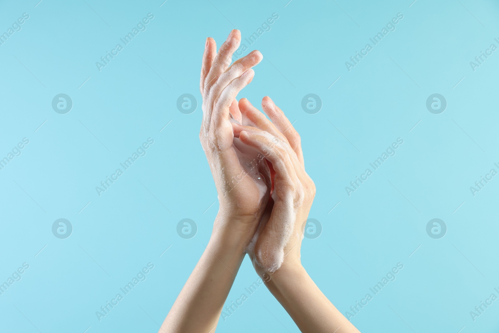 Photo of Woman washing hands with foaming soap on light blue background, closeup. Hygiene