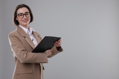 Portrait of young secretary with clipboard on grey background. Space for text