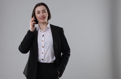 Photo of Smiling secretary talking on smartphone against grey background. Space for text