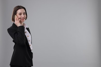 Photo of Smiling secretary talking on smartphone against grey background. Space for text