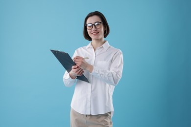 Young secretary with clipboard taking notes on light blue background