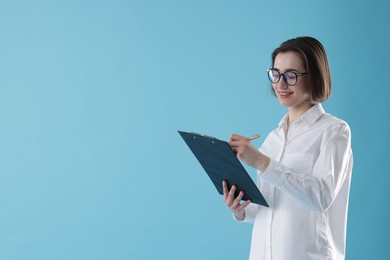 Young secretary with clipboard taking notes on light blue background. Space for text