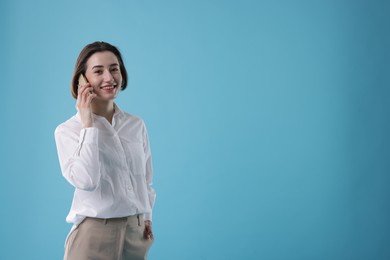 Photo of Smiling secretary talking on smartphone against light blue background. Space for text