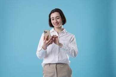 Photo of Smiling secretary using smartphone on light blue background