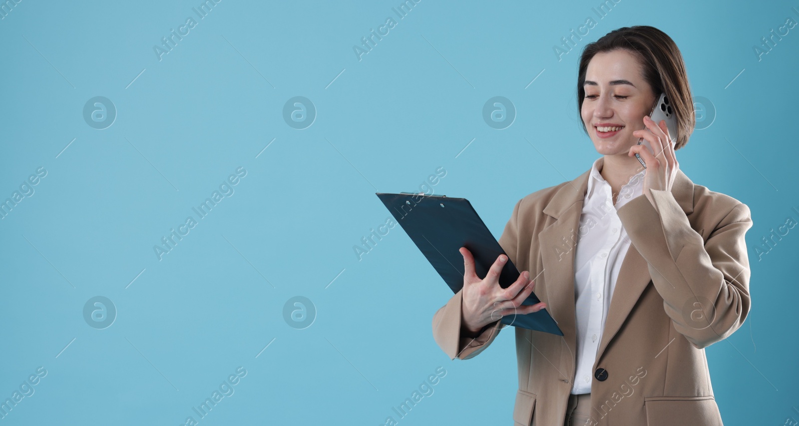 Photo of Smiling secretary with clipboard talking on smartphone against light blue background. Space for text