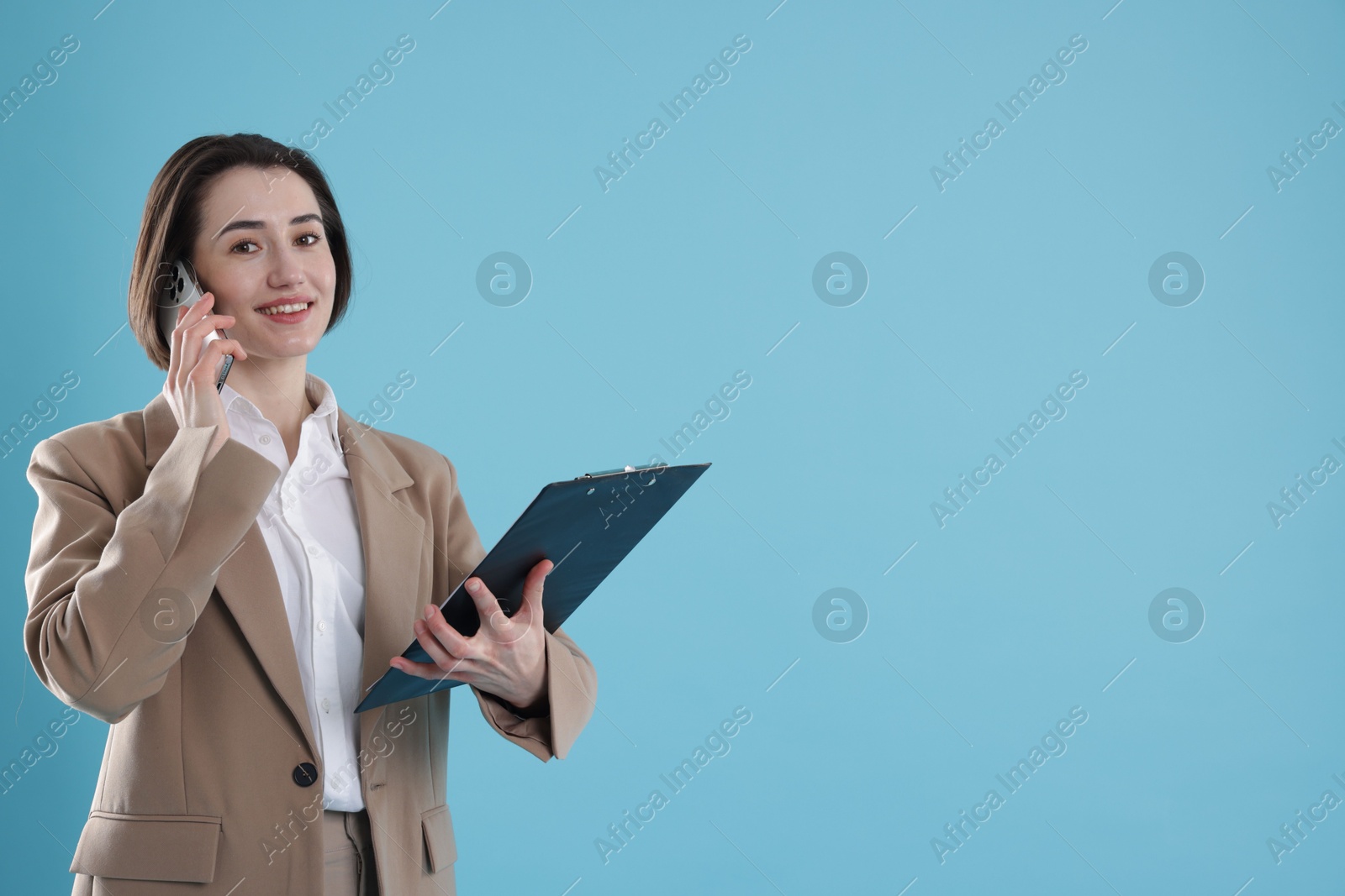 Photo of Smiling secretary with clipboard talking on smartphone against light blue background. Space for text