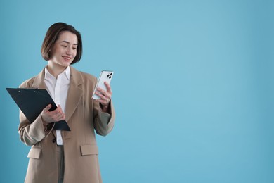 Photo of Smiling secretary with clipboard and smartphone on light blue background. Space for text