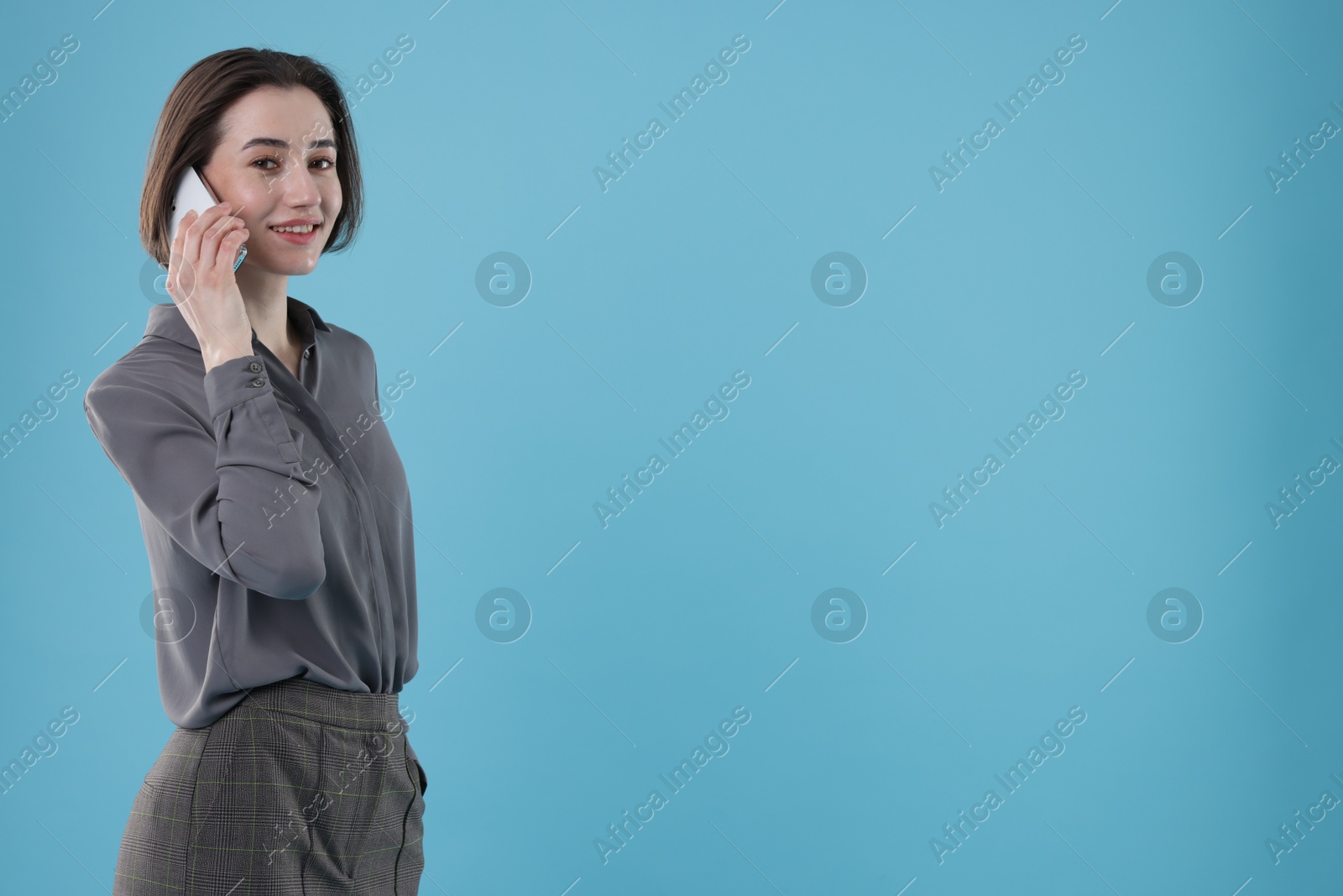 Photo of Smiling secretary talking on smartphone against light blue background. Space for text